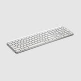 A slim white wireless computer keyboard with a matching white trackpad, shown at an angle on a light gray background.