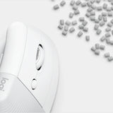 A close-up of a white Logitech computer mouse on a light gray background, with small gray rectangular pieces scattered in the upper right corner.