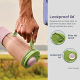 Hand holding a green and pink container with leakproof lid feature, set against a natural background.